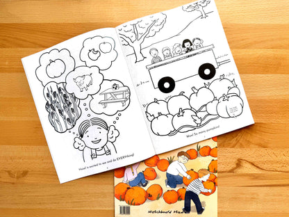 An open black-and-white children's coloring book lies on a wooden tabletop, with a second coloring book partially visible underneath. The top book shows illustrated scenes including pumpkins, a girl thinking about a pig and tractor, and a tractor loaded with children.