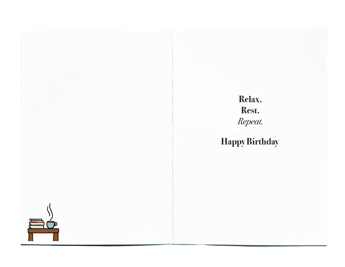 A birthday card shown open, with black text on the right reading 'Relax. Rest. Repeat. Happy Birthday, in left hand corner is a small illustration of a table with books and hot coffee in a mug on top
